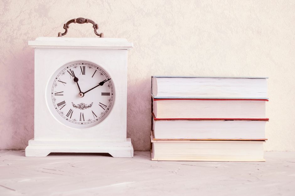 A classic white clock next to a stack of books on a rustic table. Perfect for themes of time and knowledge.